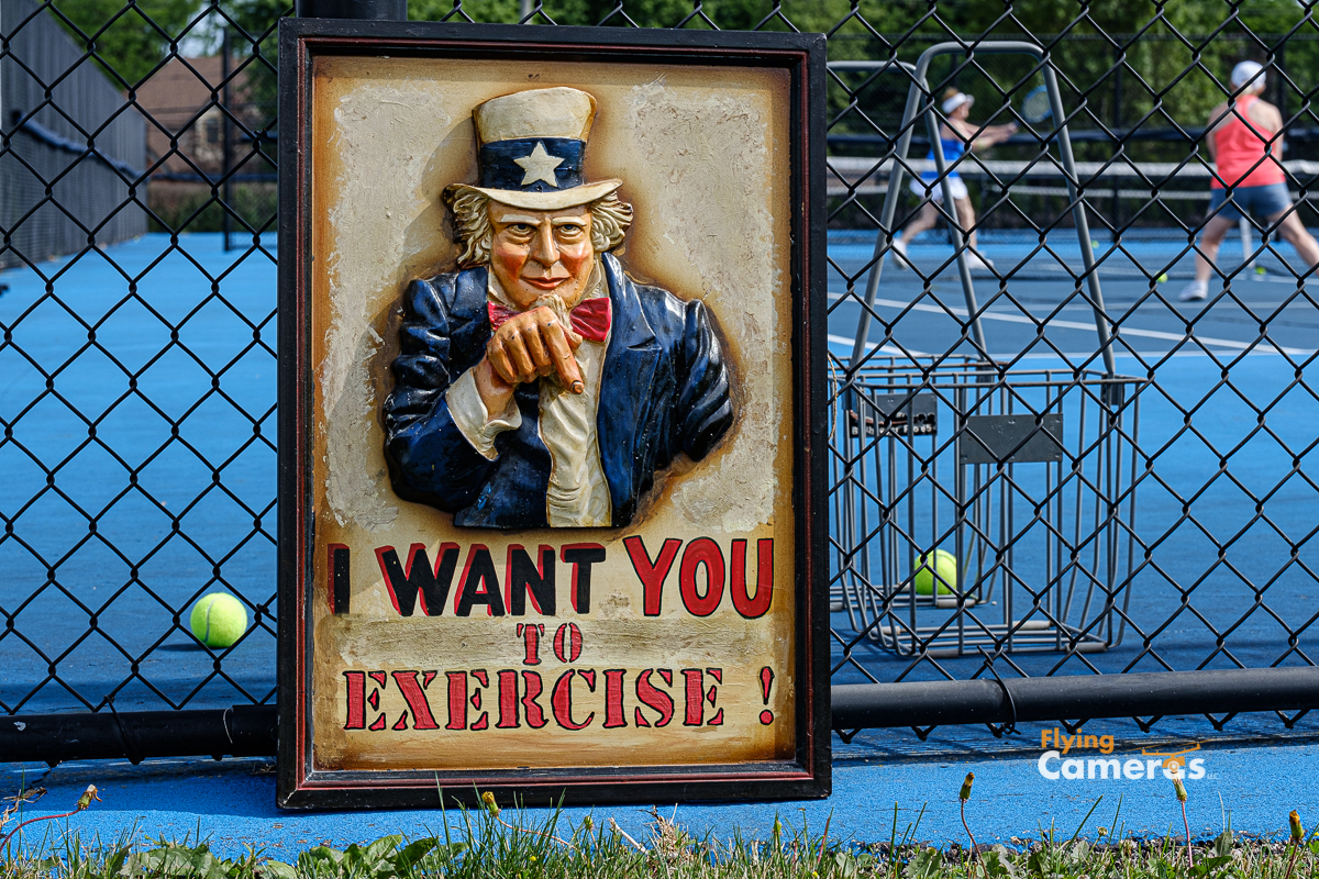 Plaster likeness of Uncle Sam directing people to exercise while a tennis match is in progress