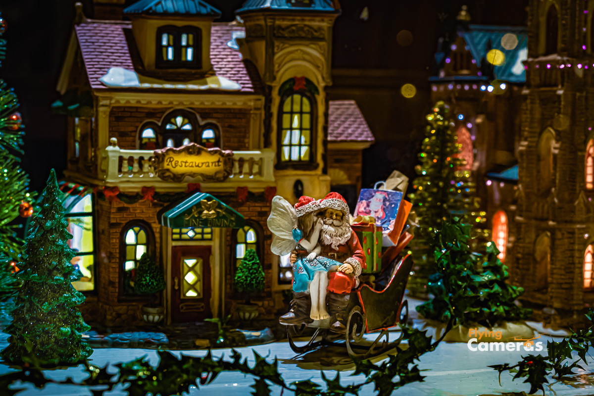 Fairy like girl sitting on Santa Claus's lap whispering in his ear - set in a holiday toy village setting